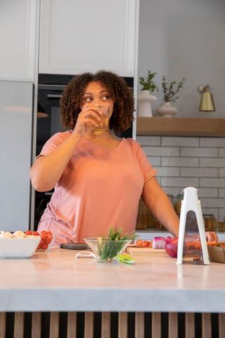 African American Woman Enjoys Refreshing Drink While Preparing Meal