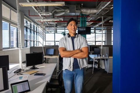Young asian man standing and smiling in modern open-plan office with headphones