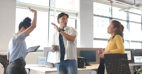 Multicultural team collaborating and celebrating in modern sunlit open-plan office