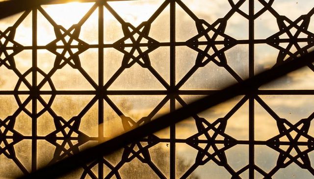 Ornate geometric lattice with star motifs framing sunrise backlight and diagonal shadow
