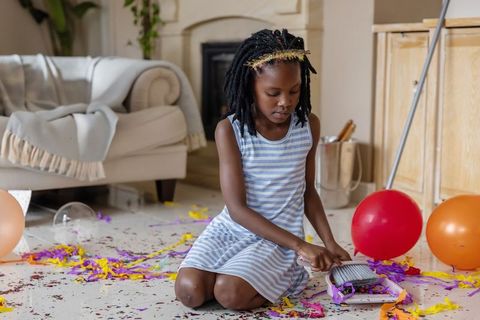 Young african american girl sweeping confetti after party in cozy living room cleanup
