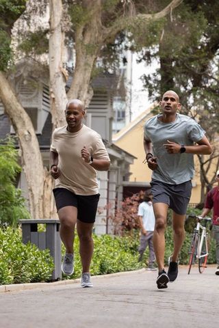 African american men jogging on tree-lined residential path wearing fitness watches