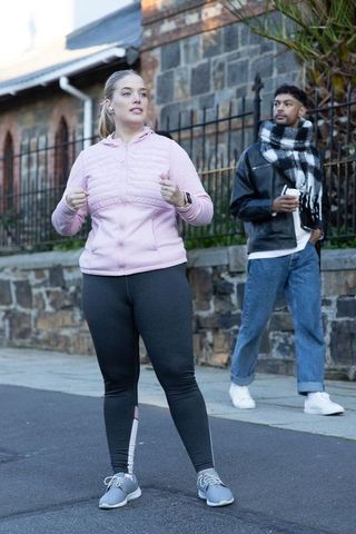 Jogging woman pausing on city sidewalk while man watches with coffee urban fitness