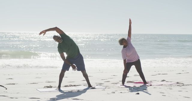 Senior couple performing stretching exercises on sunny beach. Ideal for promoting healthy lifestyles for seniors, fitness programs, and outdoor activities advertisements. Useful for illustrating the benefits of yoga and stretching in peaceful, natural environments.