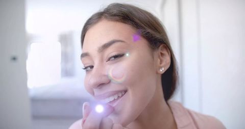Smiling woman holding led lip device in bedroom, applying beauty gadget closeup