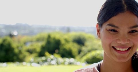 Woman Smiling in Sunlit Park with Abstract Green Background