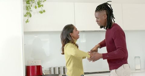 Indian woman and African American man holding hands smiling in modern sunlit kitchen