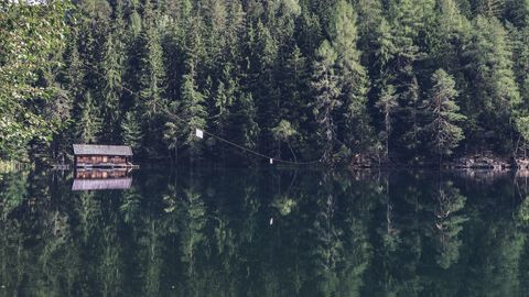 Rustic boathouse on glassy forest lake reflecting evergreen trees and tranquil wilderness