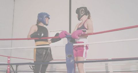 Two female boxers leaning on ropes sparring in ring wearing headgear and gloves