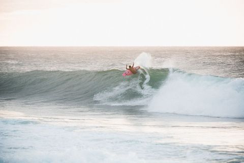 Surfer riding clear ocean wave at sunset