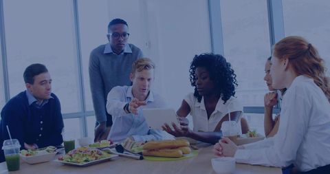 Multicultural team collaborating over tablet during working lunch in modern office