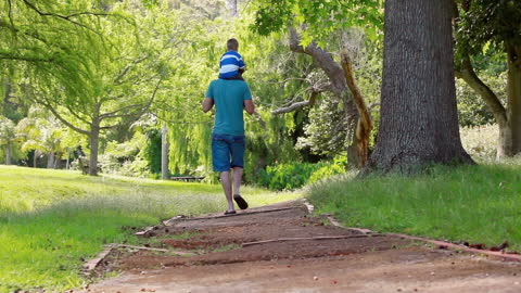 Father Carrying Son on Shoulders Through Scenic Park