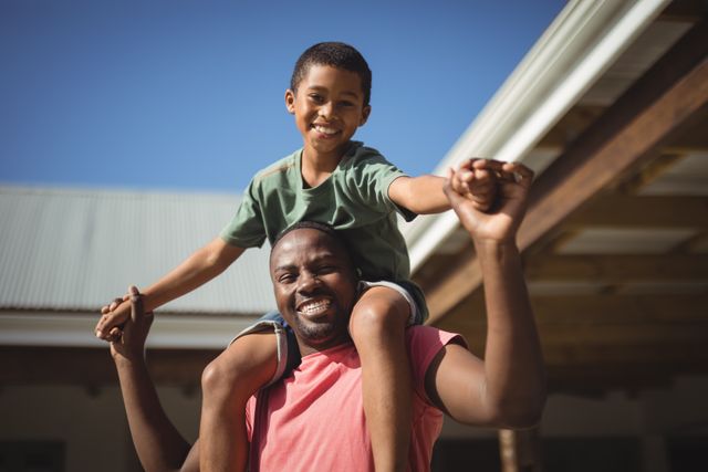 Father carrying son on shoulders, both smiling and enjoying time together outdoors. Perfect for use in family-oriented advertisements, parenting blogs, and promotional materials highlighting family bonding and happiness.