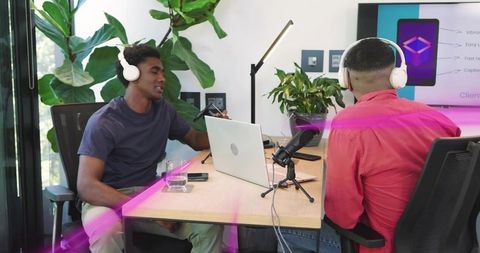 Recording podcast cohosts collaborating in modern studio with headphones and laptop