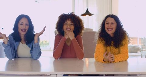 Diverse female friends smiling at sunlit kitchen countertop, casual lifestyle
