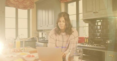 Woman In Bright Kitchen Using Laptop While Preparing Breakfast