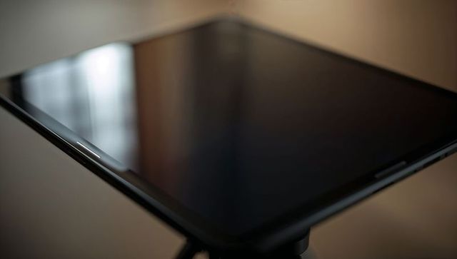 Sleek black tablet sitting on mini tripod reflecting window light with glossy bezel