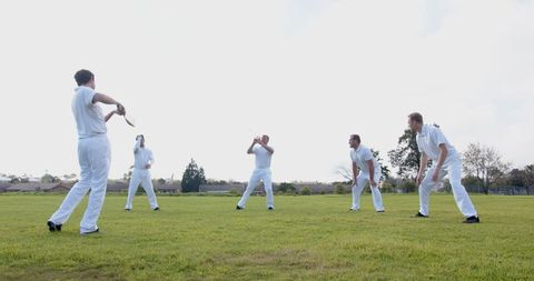 Male cricket players practicing fielding drill on lawn