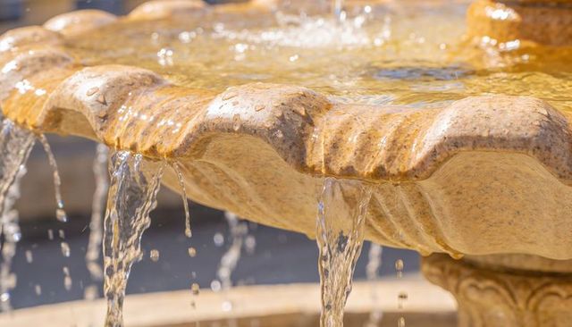 Sunlit carved stone fountain spilling water over scalloped rim in courtyard