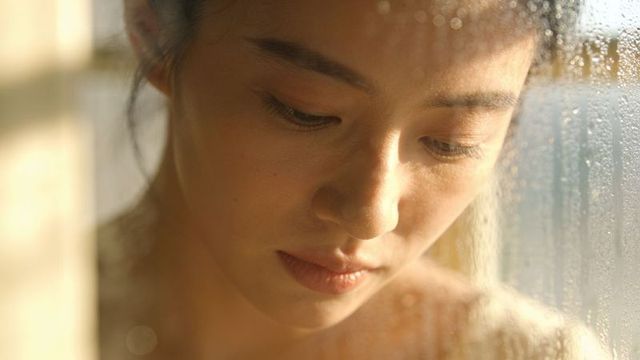 Gazing asian woman leaning by window during golden hour soft portrait with condensation