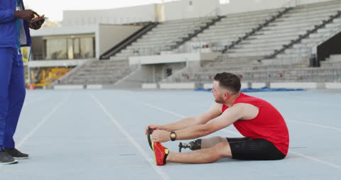 Disabled athlete with a blade prosthetic is stretching on a running track alongside a coach, emphasizing training and perseverance. Use for inspirational sports campaigns, inclusive fitness programs, and showcasing diversity in athletics.