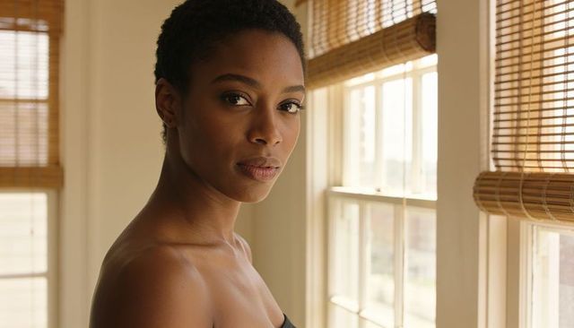 Confident woman posing by sunlit window in black strapless top, natural headshot
