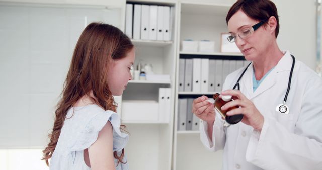 Female doctor interacts with young girl, possibly preparing to give medication in a medical office. Stethoscope around doctor's neck signifies healthcare environment. Scene shows commitment to patient care and supportive healthcare environment. Useful for articles about pediatric healthcare, medical treatments, or professional medical consultations for children.