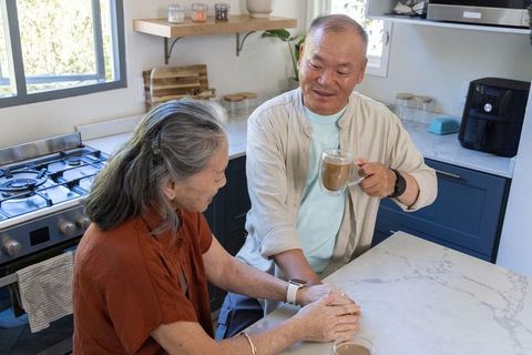 Senior asian couple sharing coffee and holding hands at marble kitchen island, intimate