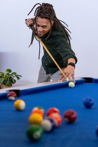 African american man leaning and aiming cue on blue-felt pool table, focused play