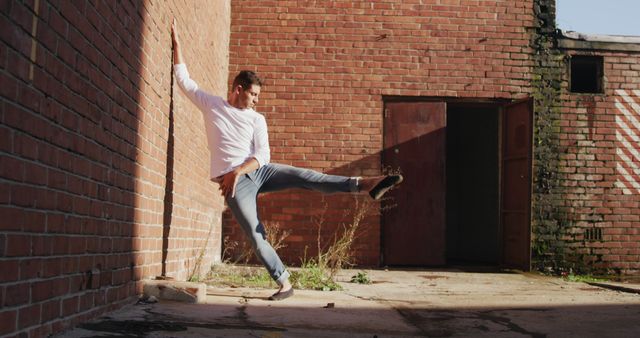 Caucasian male dancer dancing in sunny brick courtyard, copy space. Dance, urban lifestyle and movement, unaltered.