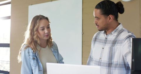 Collaborating coworkers reviewing plans on laptop and whiteboard in sunlit modern office