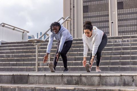 Diverse friends stretching on city steps before outdoor run, urban fitness training