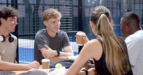 Diverse friends chatting and enjoying coffee near padel court