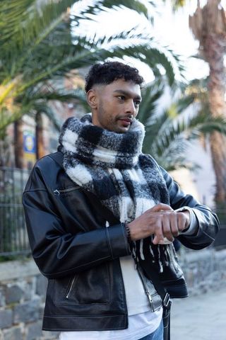 Asian man wearing leather jacket and plaid scarf checking watch on palm-lined street