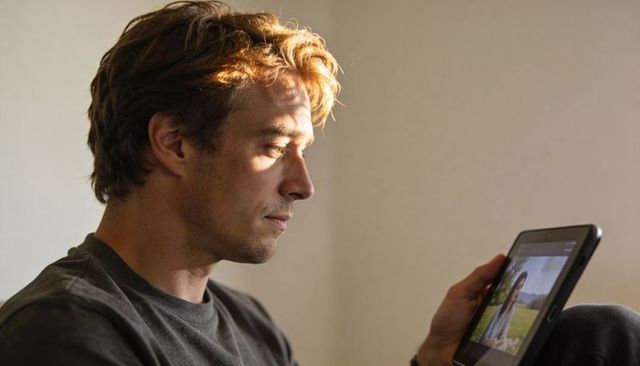 Adult man studying on tablet in quiet home, holding device and focusing on screen in warm light