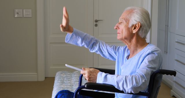 Elderly man sitting in a wheelchair waving and holding a book. This scene can depict themes related to aging, health care, thoughtful reflection, and staying chronic invalid. Ideal for usage in content dealing with elderly care services, independence in elderly, patients stories, or senior living arrangements.