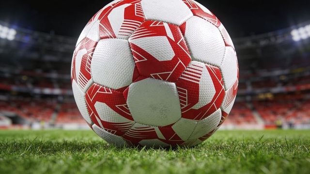 Close-up red-and-white soccer ball resting on trimmed turf under stadium floodlights