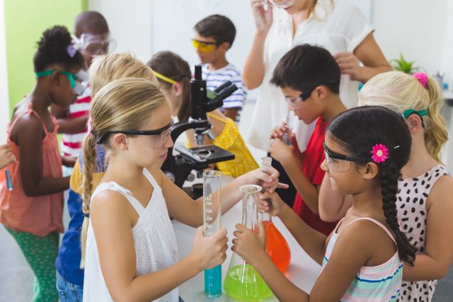 Children of various ethnic backgrounds are conducting a science experiment in a classroom laboratory. They are wearing safety goggles and using beakers and test tubes, indicating a focus on hands-on learning and teamwork. This image is ideal for educational materials, school websites, and STEM program promotions.