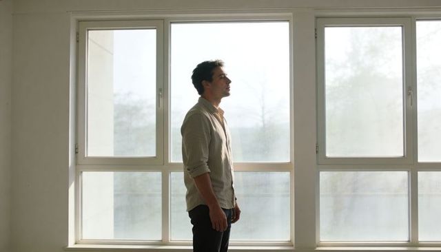 Man gazing through large window in minimalist sunlit interior, contemplative lifestyle