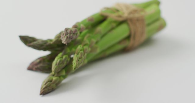 Fresh bundle of green asparagus tied with twine on white background. Perfect for illustrating themes of healthy eating, organic food, vegetarian and vegan diets, nutrition, and culinary arts. Useful for food blogs, recipe websites, grocery store advertisements, and nutrition articles.