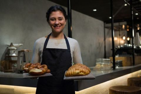 Smiling artisan baker presenting freshly baked goods in warm rustic bakery
