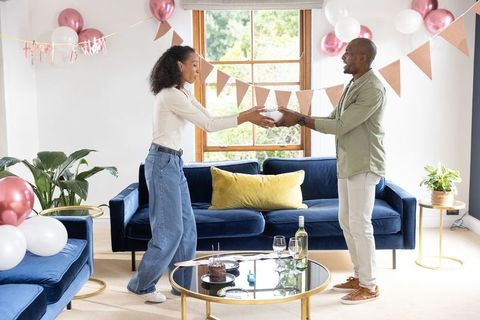 Diverse couple exchanging gift during intimate home birthday celebration in sunlit room