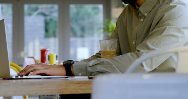 A young Asian man is working on a laptop at a home office, with copy space. His focus and casual attire suggest a comfortable yet productive remote work environment.