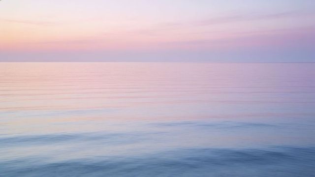 Pastel dawn over calm sea minimalist seascape with soft ripples, tranquil sunrise glow