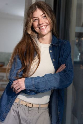 Sunlit woman smiling and leaning by glass door in casual denim outfit, home lifestyle