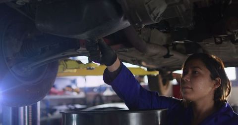 Mid adult female mechanic draining engine oil in garage
