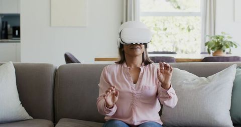 Mature woman enjoying immersive VR headset experience on sofa in modern bright living room