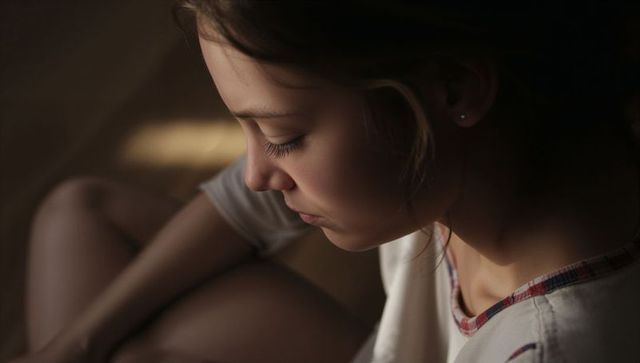 Teen sitting curled up lowering head toward knees intimate warm portrait with stud earring