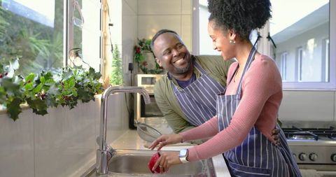 Couple washing bell pepper together in sunlit kitchen, sharing cozy holiday cooking moment