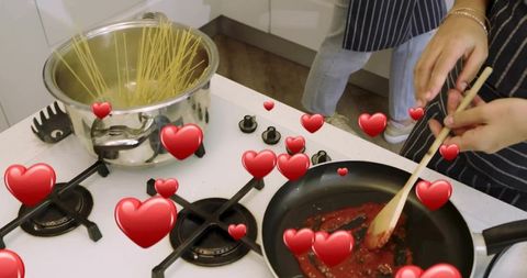 Couple cooking together stirring tomato sauce boiling spaghetti on gas stove with hearts